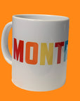 A white ceramic mug with the word 'MONTREAL' printed in multicolored bold letters.