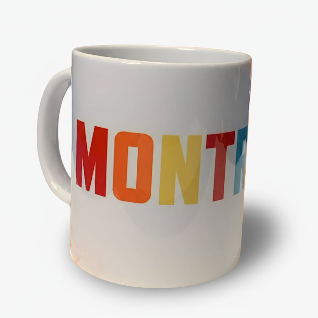 A white ceramic mug with the word 'MONTREAL' printed in multicolored bold letters.