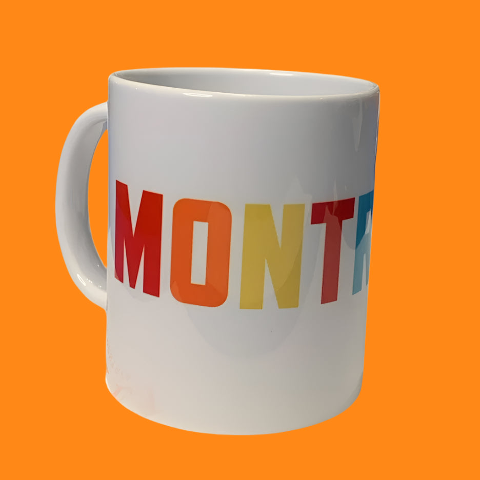 A white ceramic mug with the word 'MONTREAL' printed in multicolored bold letters.